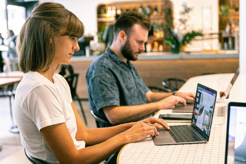 Dos personas trabajando en sus ordenadores portátiles en un café moderno o espacio de co-working.